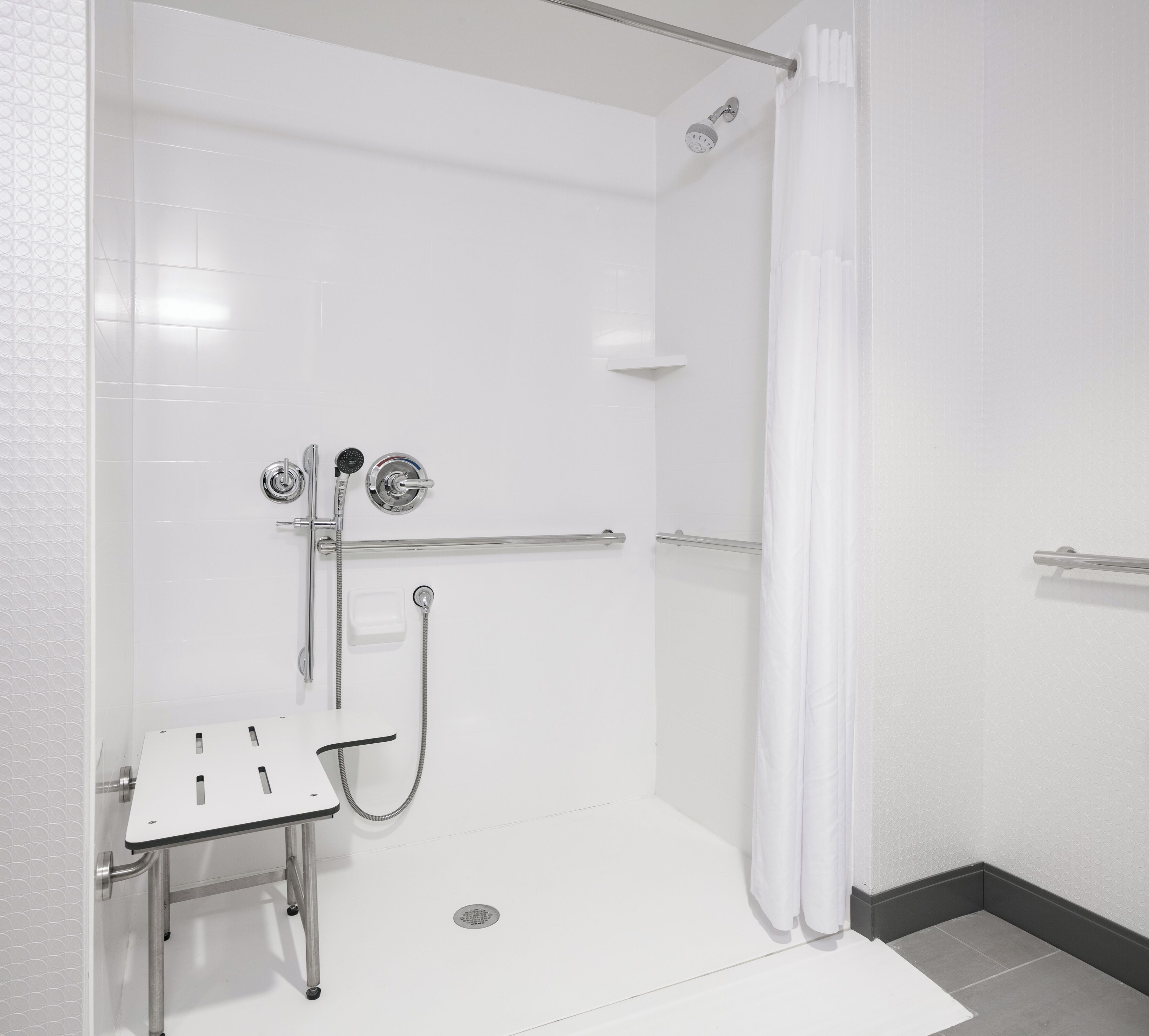 A modern shower area with a glass door, a handheld showerhead, a fixed showerhead, and a handheld shower attachment.