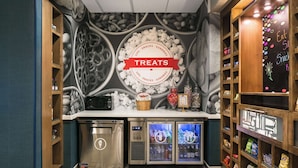 A kitchen area with a 'Treats' sign, a microwave, a dishwasher, and a refrigerator with a beverage display. - Hampton Inn Wichita Northwest (Wichita)