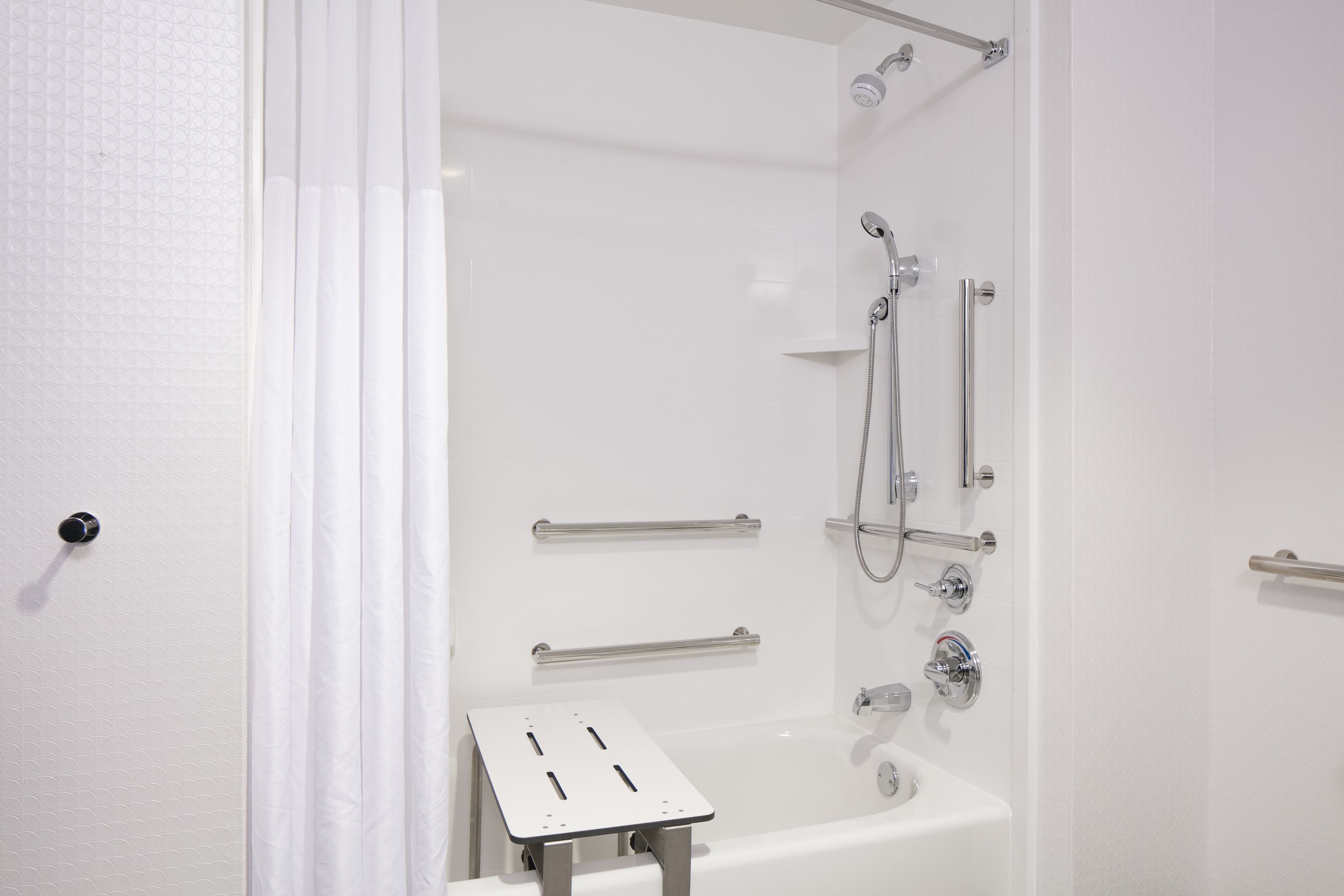 Un baño moderno con cabina de ducha, barras de apoyo y un lavamanos blanco.