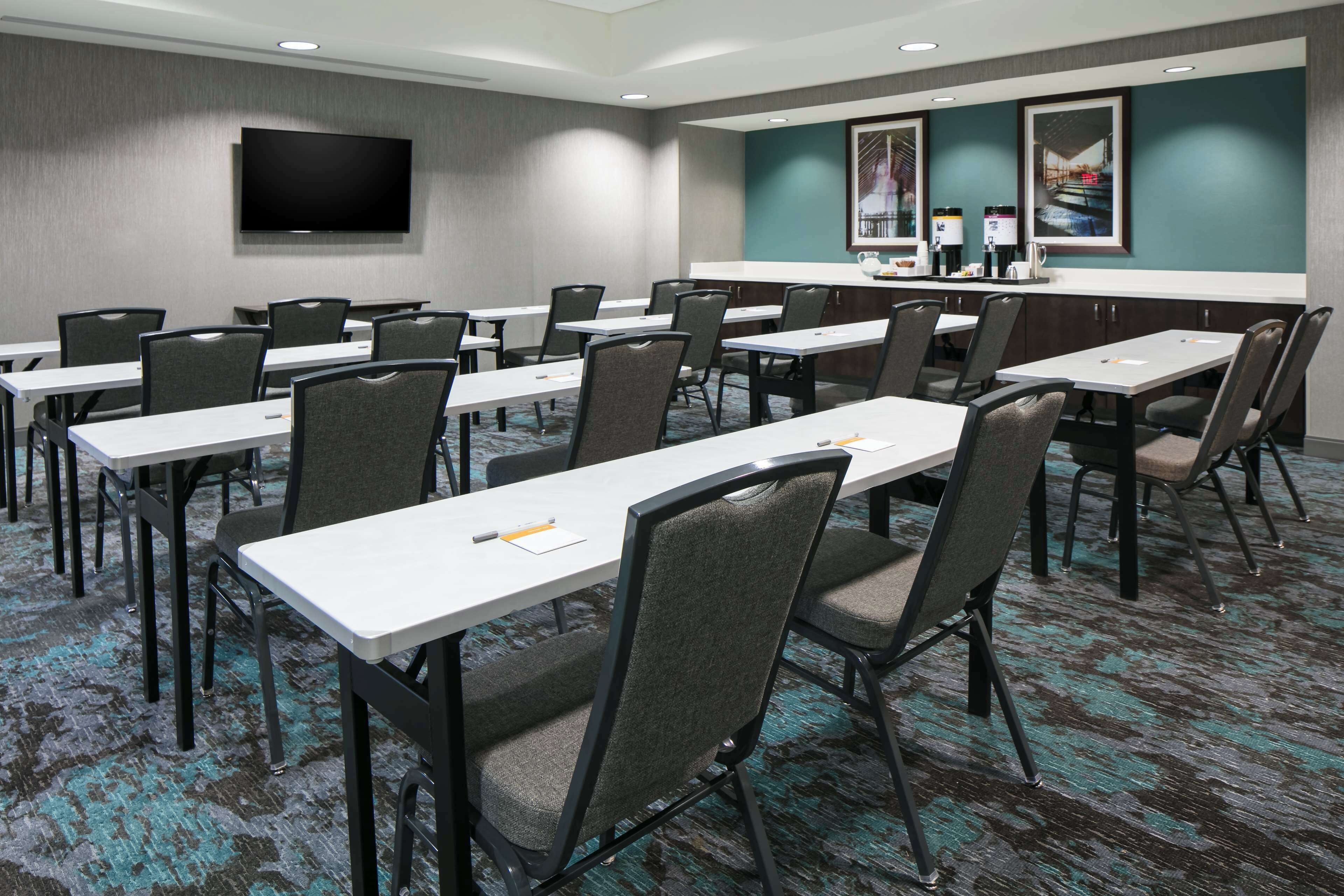 A conference room with multiple tables and chairs, a flat-screen TV mounted on the wall, and a counter with amenities.
