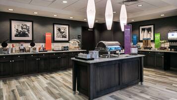 A modern kitchen area with a central island, dark cabinetry, and various food service equipment.