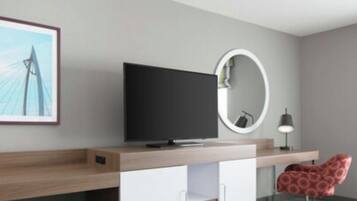 A modern room with a flat-screen TV on a wooden desk, a round mirror, and a red chair.