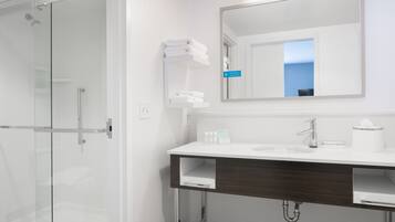 A modern bathroom with a glass shower enclosure, a white sink with a dark wood vanity, and a mirror above the sink.