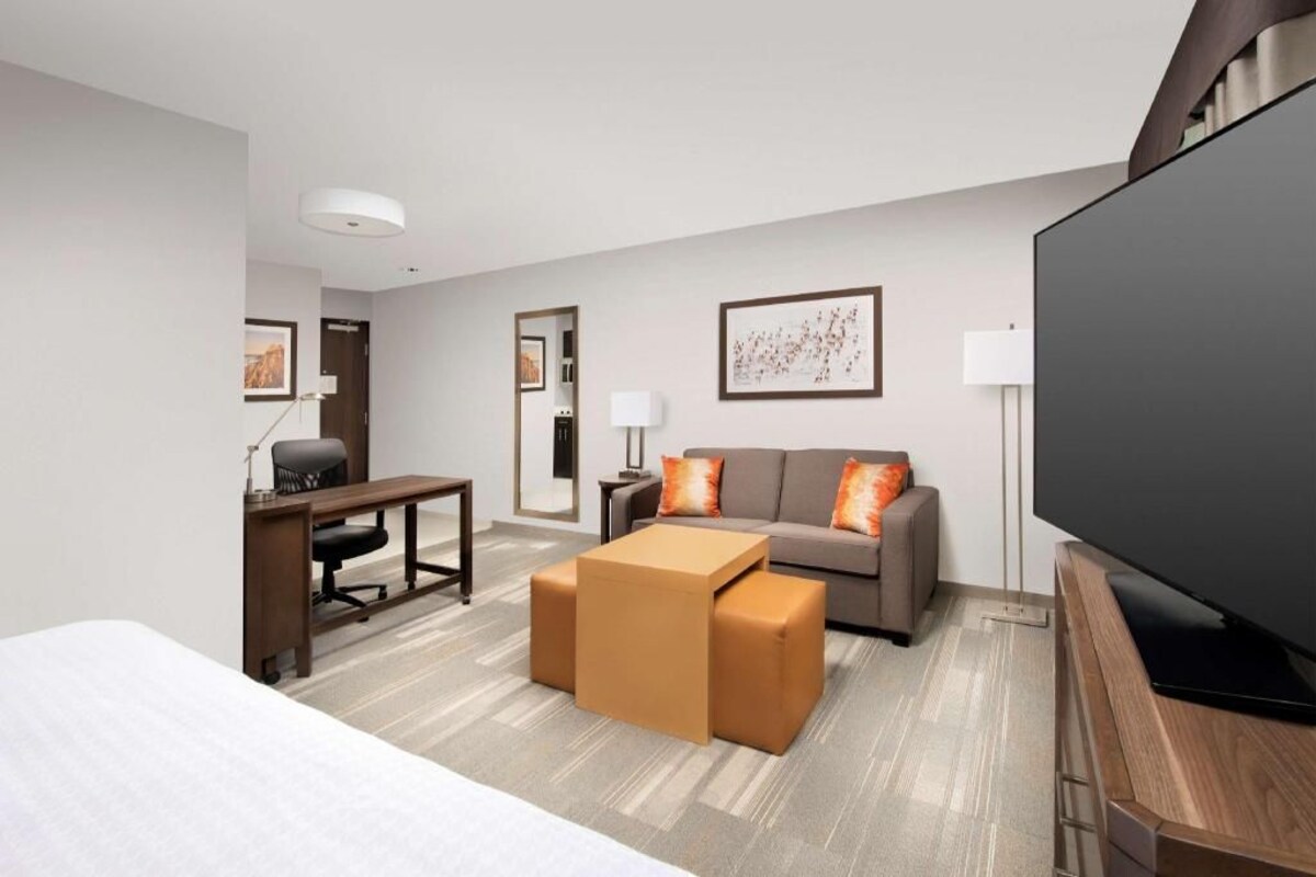 A modern hotel room with a bed, a sofa, a desk, a television, and a large window.