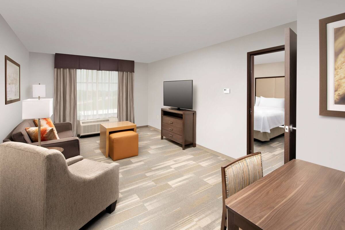 A hotel room with a sofa, ottoman, TV, and a bed with a headboard.