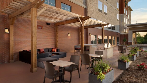 An outdoor patio area with seating and a bar, surrounded by brick walls and wooden pergolas. - Homewood Suites by Hilton Kansas City Speedway (Kansas City)