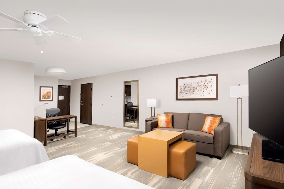 A hotel room with a bed, a desk, a sofa, a coffee table, a TV, and a ceiling fan.