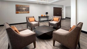 A modern lounge area with four armchairs, a central coffee table, and a chandelier. - Homewood Suites by Hilton Kansas City Speedway (Kansas City)
