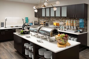 A modern kitchen with a buffet setup, including a grill, coffee machines, and a fruit bowl.