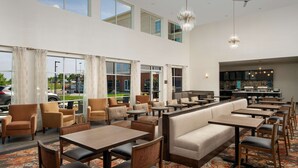 A spacious hotel lobby with multiple seating areas, including sofas and tables, and a visible kitchen area in the background. - Homewood Suites by Hilton Kansas City Speedway (Kansas City)