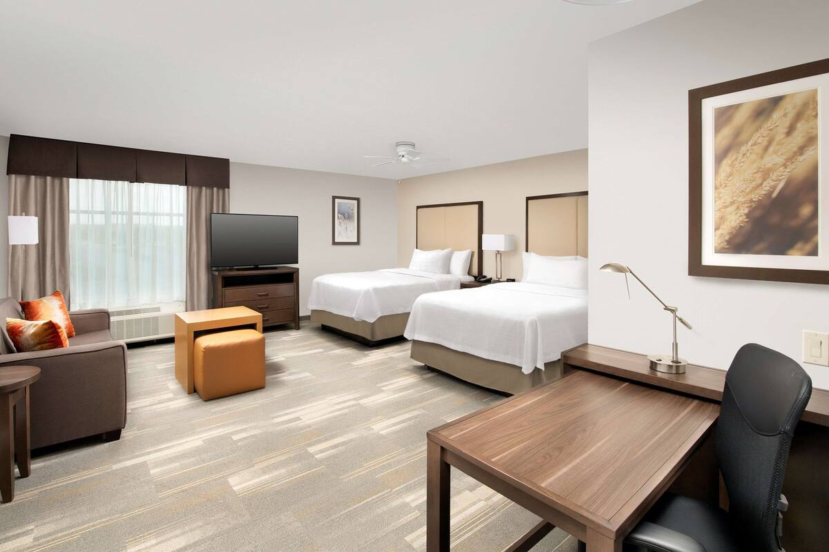 A hotel room with a bed, a desk, a chair, a TV, and a window with curtains.