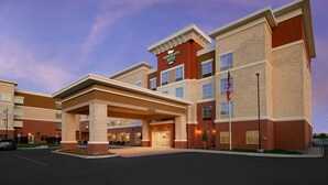 A hotel with a brick facade, a covered entrance, and an American flag. - Homewood Suites by Hilton Kansas City Speedway (Kansas City)