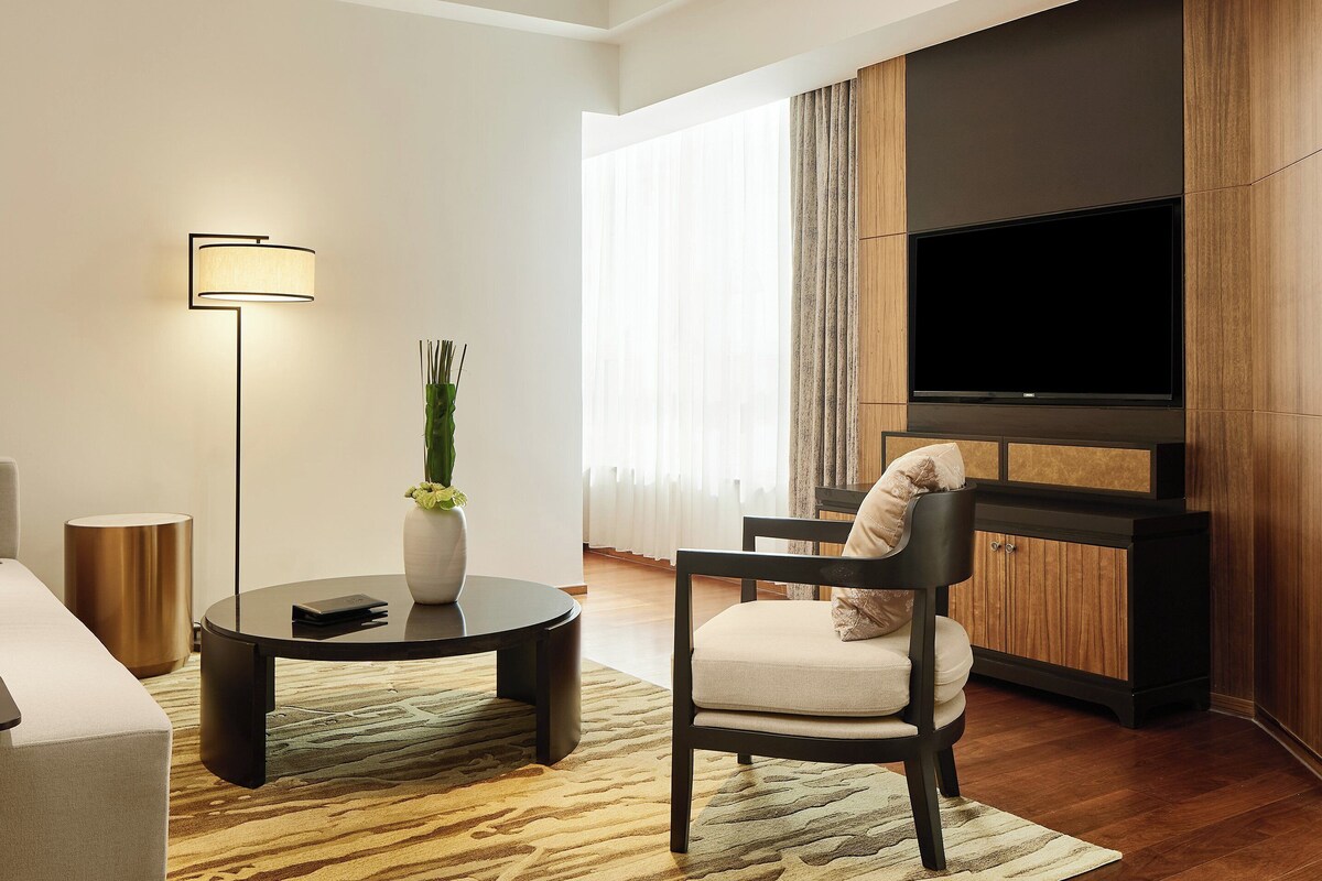 A modern living room with a sofa, a coffee table, a chair, a floor lamp, a TV, and a large window with curtains.