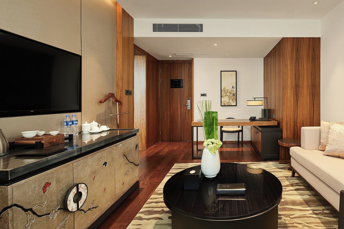A modern living room with a flat-screen TV, a coffee table with a vase, a sofa, and a desk with a lamp.