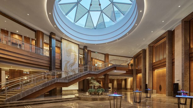 A spacious hotel lobby with a central staircase, a large skylight, and multiple levels. - HUALUXE Ningbo Harbor City by IHG (Ningbo)