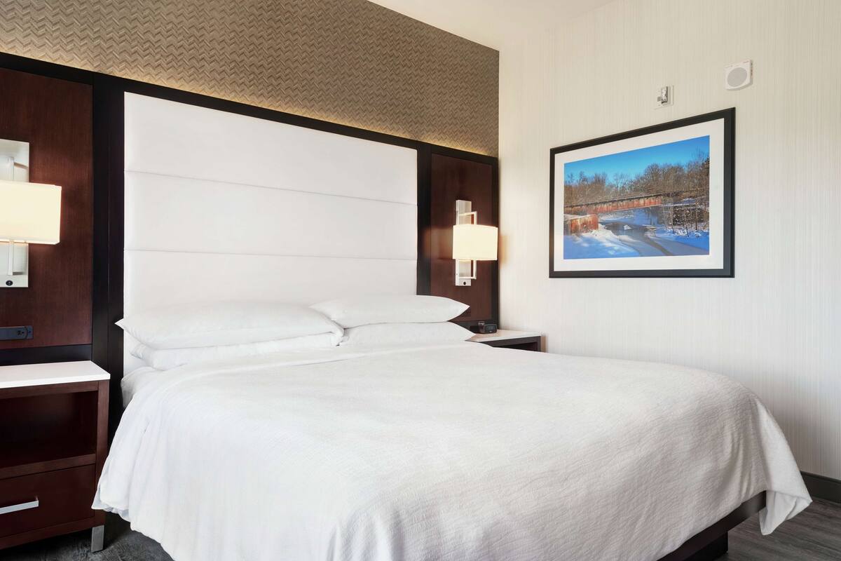 Un lit bien fait, avec du linge de lit blanc, dans une chambre d’hôtel.
