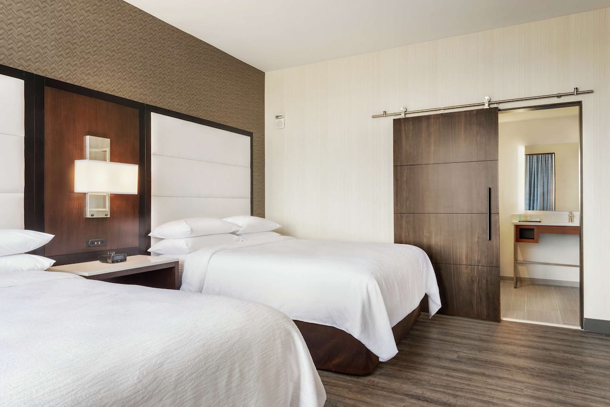 Une chambre d’hôtel avec deux lits, une table de chevet avec une lampe, un grand miroir et une armoire avec une porte coulissante.