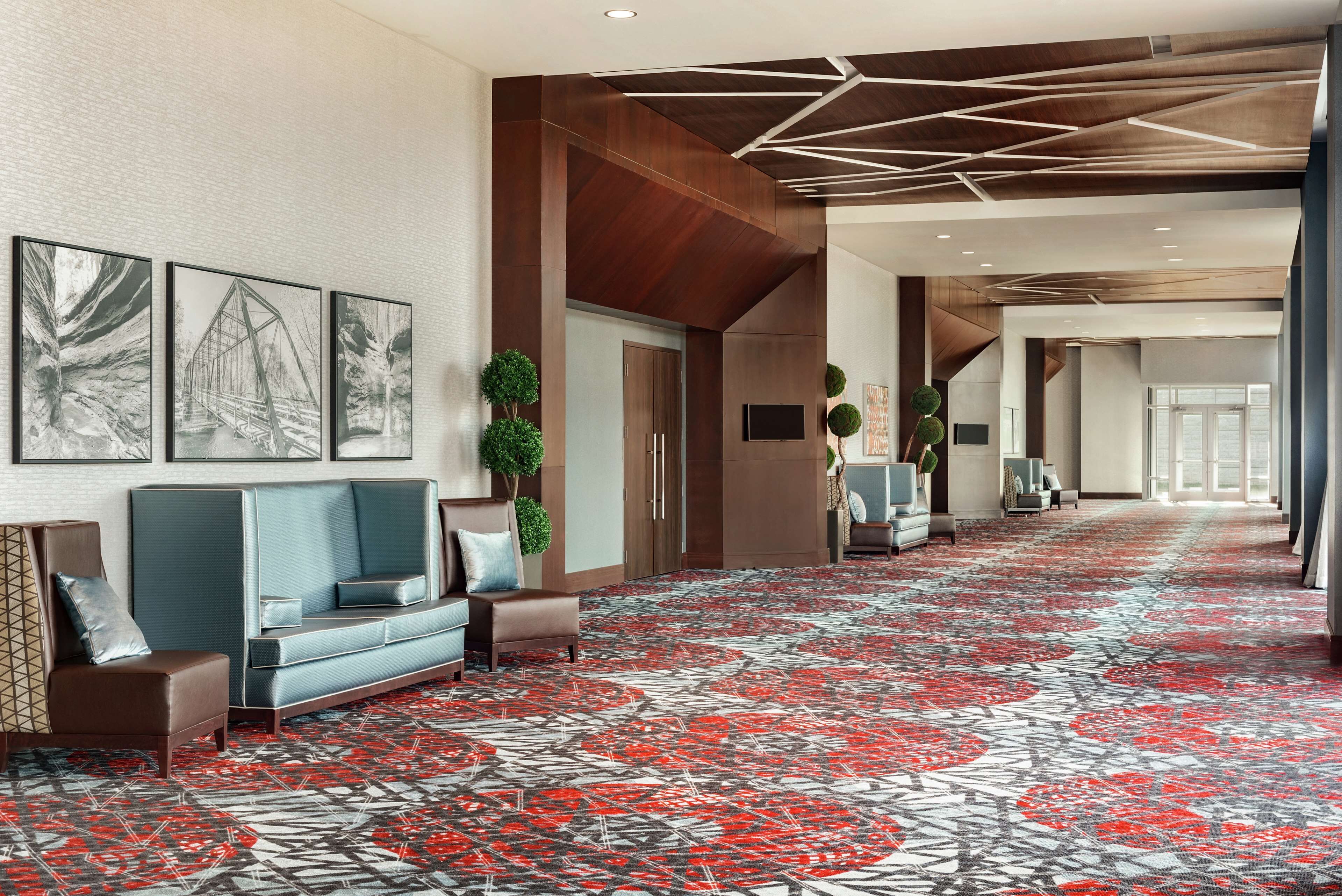 A hotel lobby with a patterned carpet, seating area, artwork on the walls, and a modern ceiling design.