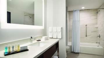 Un baño moderno con un espejo grande, un lavamanos con artículos de aseo, una ducha y una bañera.