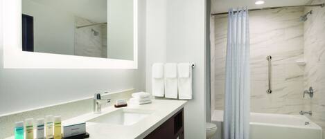 A modern bathroom with a large mirror, a sink with toiletries, a shower, and a bathtub.