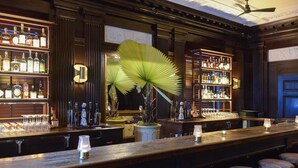 Un espace bar avec des étagères en bois remplies de bouteilles, un grand ventilateur et des tabourets de bar.