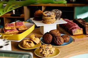 A variety of baked goods displayed on a wooden table, including cookies, muffins, and pastries.