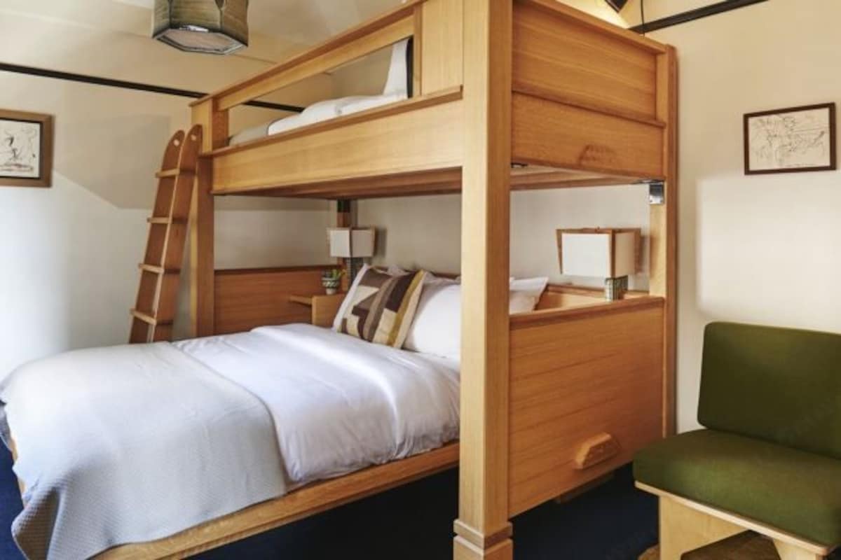 A bunk bed with a ladder, a bedside table with a lamp, and a green chair.
