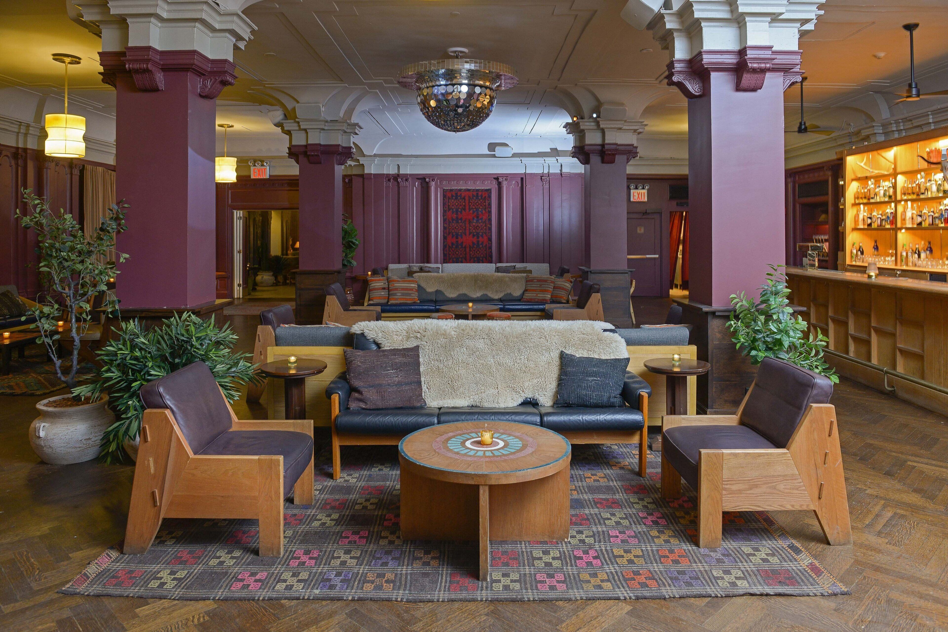 Um hall com sofás, cadeiras de madeira, uma mesa de centro redonda e um espaço de bar com prateleiras de garrafas.