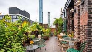 Une terrasse sur le toit, avec des carreaux hexagonaux, des chaises en métal vert et des plantes en pot.