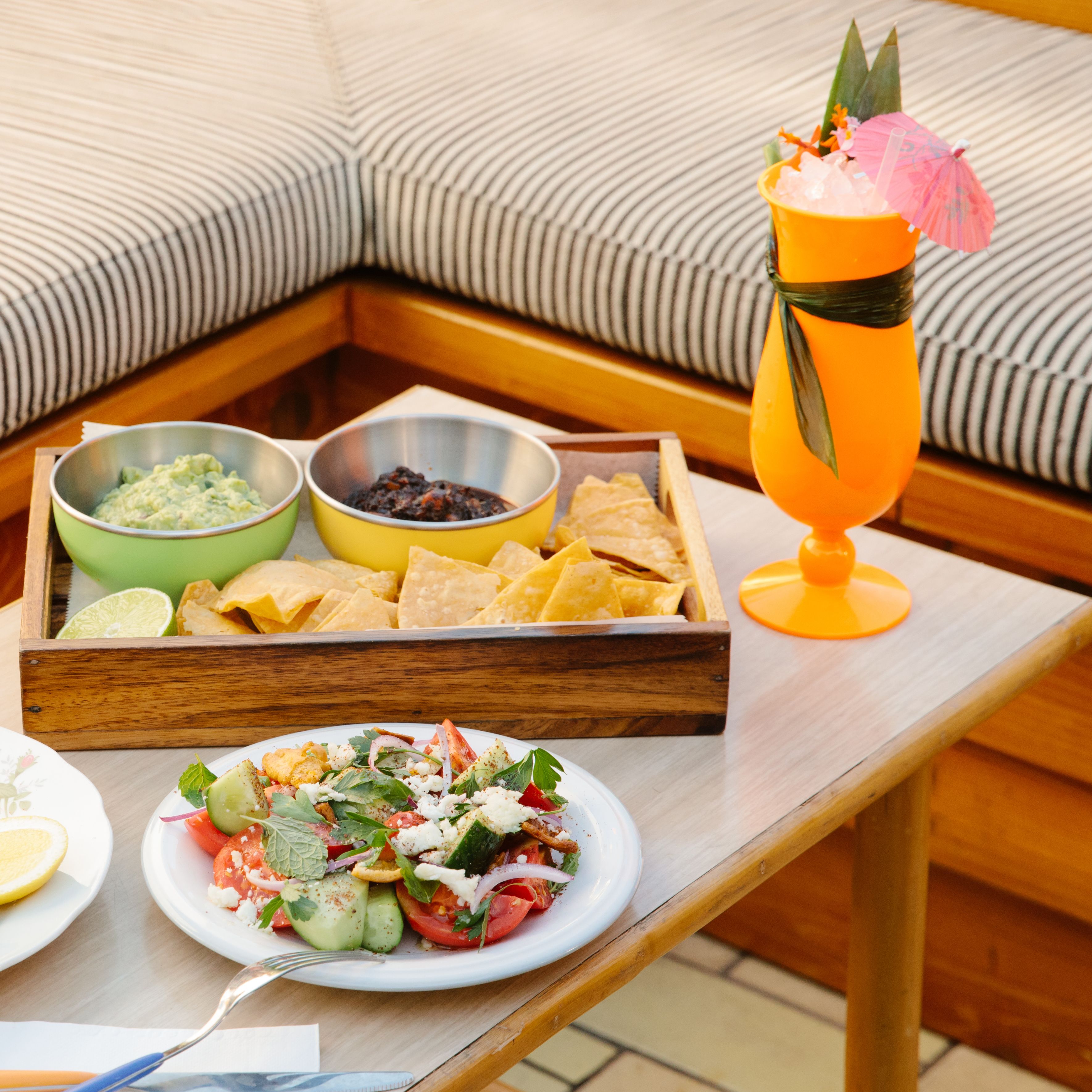Une table à manger avec un plateau de chips, des bols de sauces et une boisson servie avec une paille.