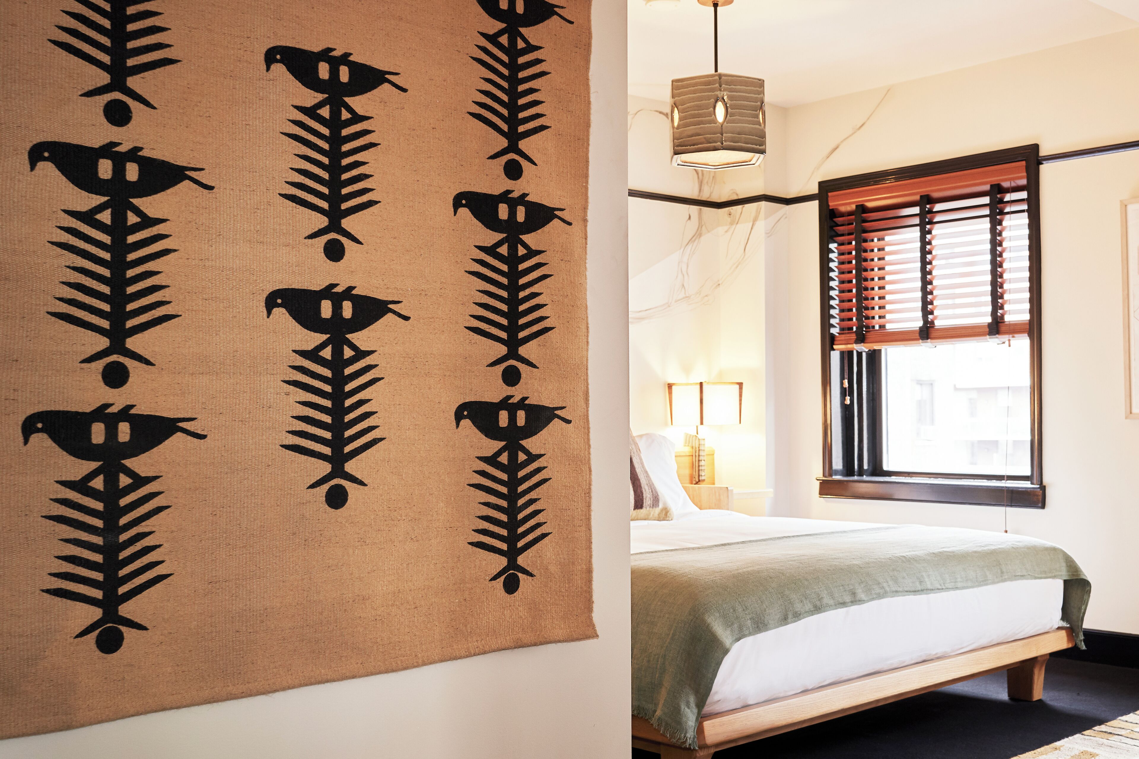 Una habitación con una cama, una ventana con persianas, una lámpara colgante y un tapiz decorativo en la pared.