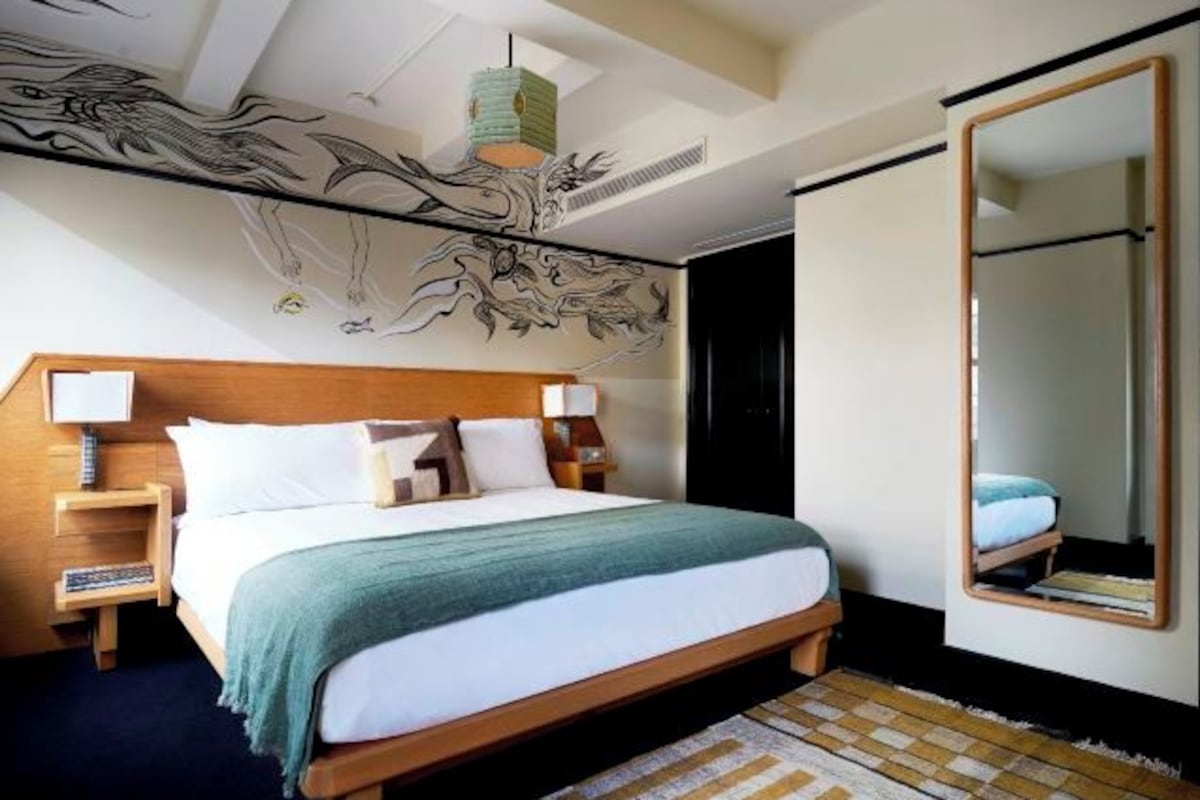 A modern hotel room with a large bed, a wooden headboard, a large mirror, and a unique wall art piece.