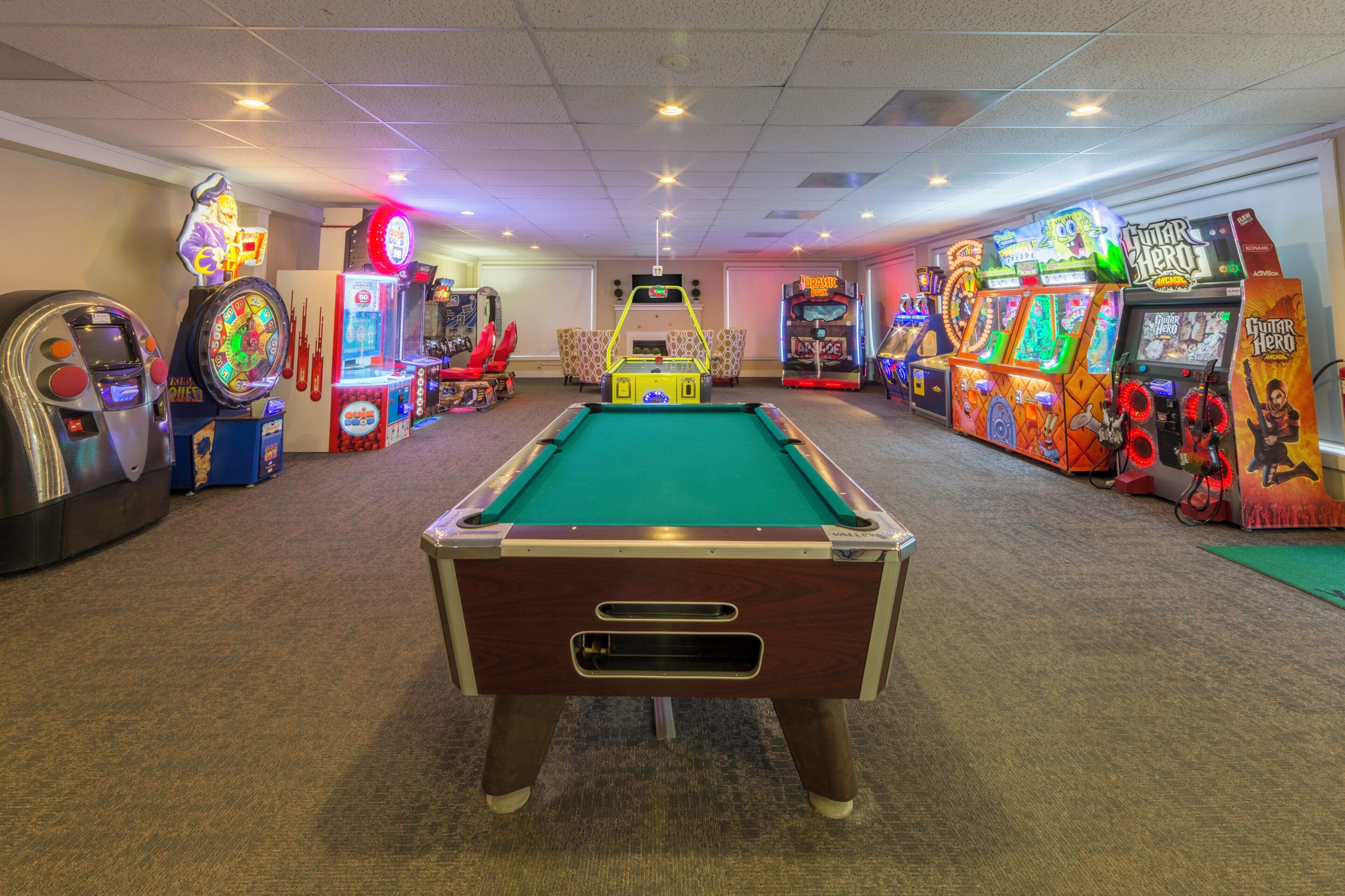 Une table de billard est placée au centre d’une pièce, de part et d’autre de laquelle se trouvent des jeux d’arcade.