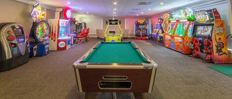 A pool table in the center of a room with arcade games on either side.
