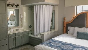 A hotel room with a large bed, a bathroom with a bathtub, a vanity with a mirror, and a window with curtains. - Holiday Inn Club Vacations Oak 'n Spruce Resort (South Lee)