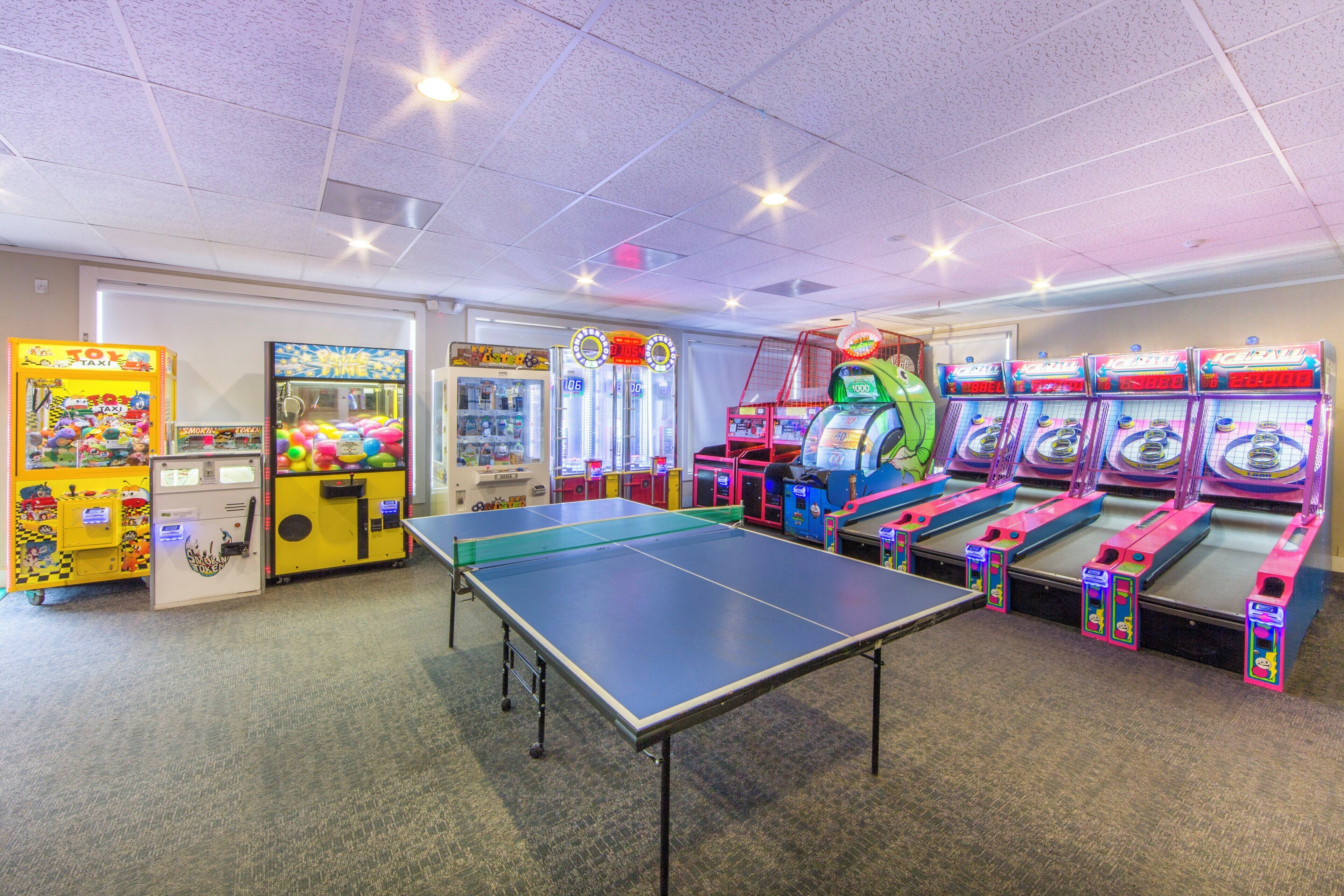 Un salón de juegos interior con diversas máquinas recreativas, una mesa de ping pong y un expendedor.