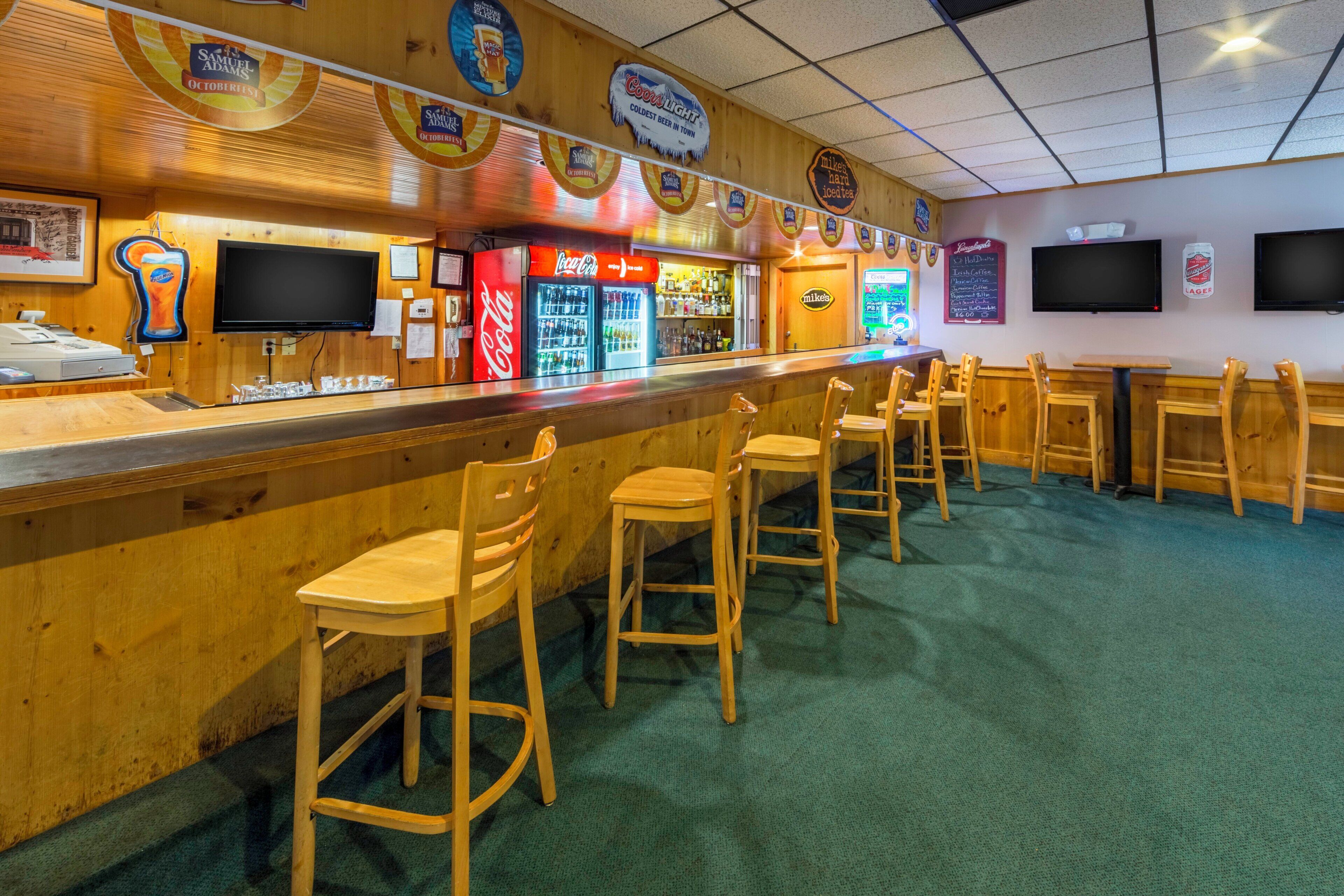 A bar area with wooden bar stools, a Coca-Cola refrigerator, and various beer taps.