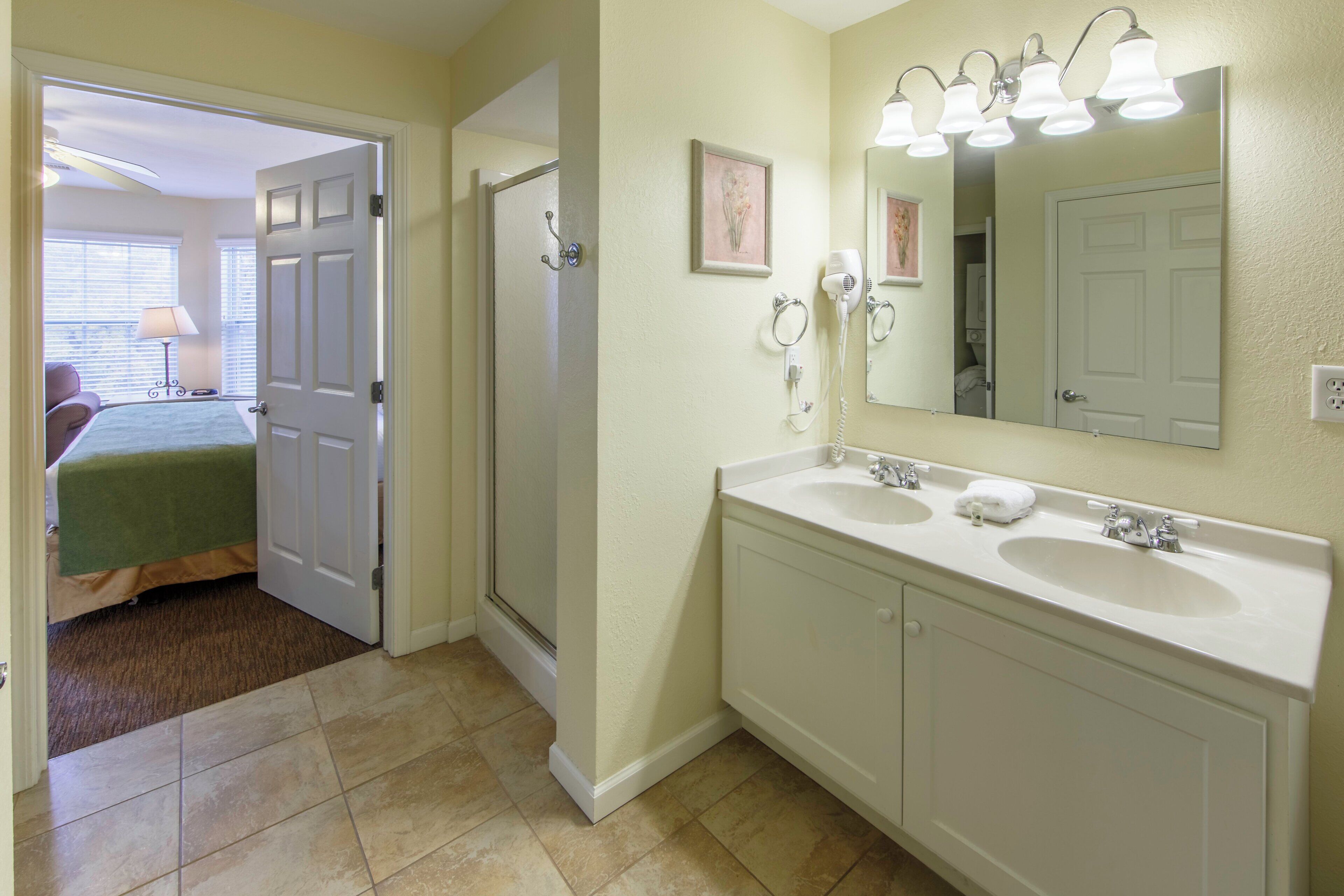 A bathroom with two sinks, a mirror, and a hairdryer on the wall.