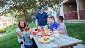 A family dining outdoors at a wooden picnic table with various food items. - Holiday Inn Club Vacations Oak 'n Spruce Resort (South Lee)