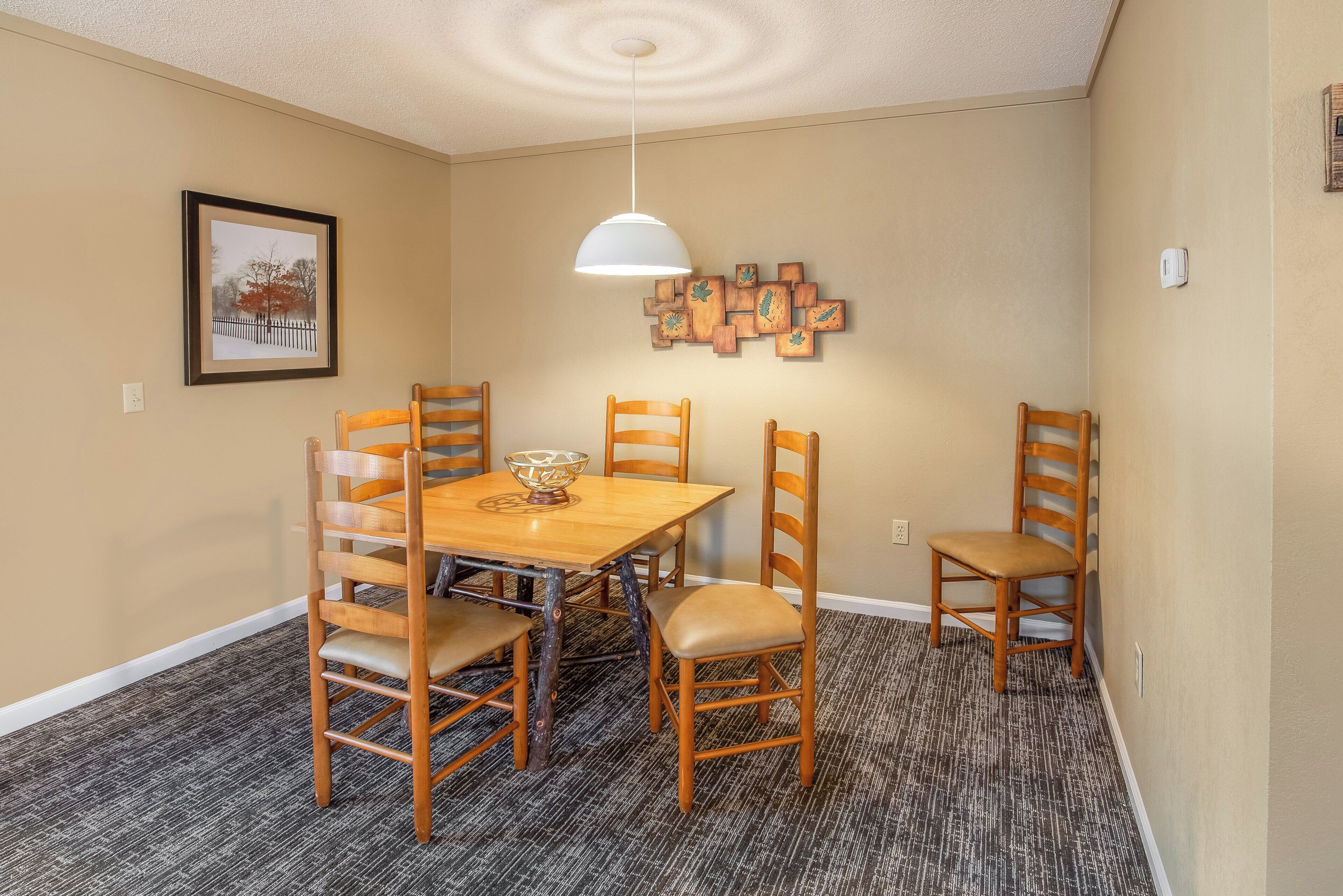 Un coin repas avec une table et des chaises en bois, un luminaire fixé au mur et un tableau encadré.