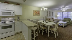 A kitchen with white cabinets, a microwave, and a stove. There is a dining table with chairs and a chandelier. A sofa and armchair are in the living area. - Holiday Inn Club Vacations Oak 'n Spruce Resort (South Lee)