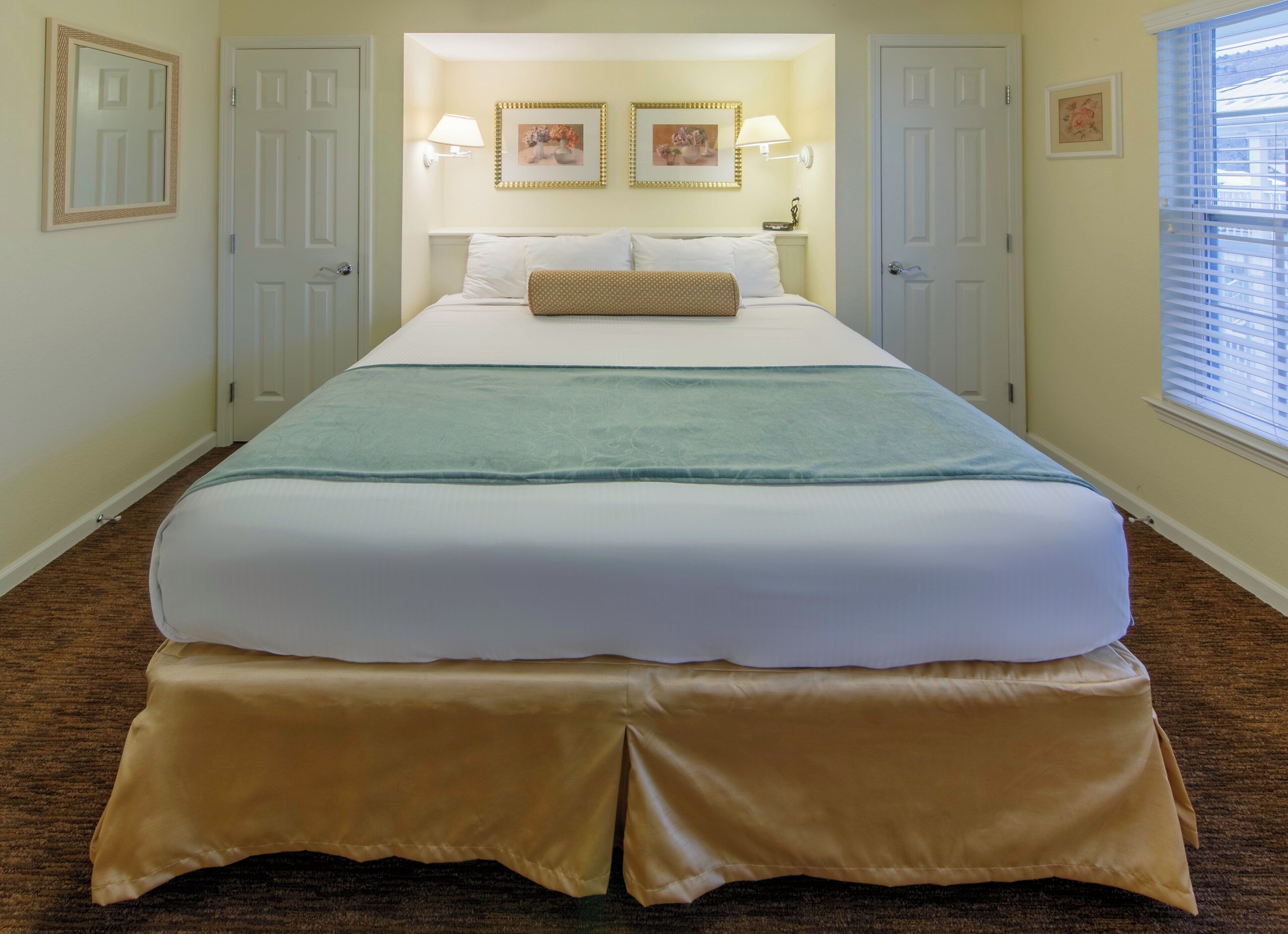 Quarto de hotel com uma cama grande, duas luminárias na parede e uma janela com persianas.