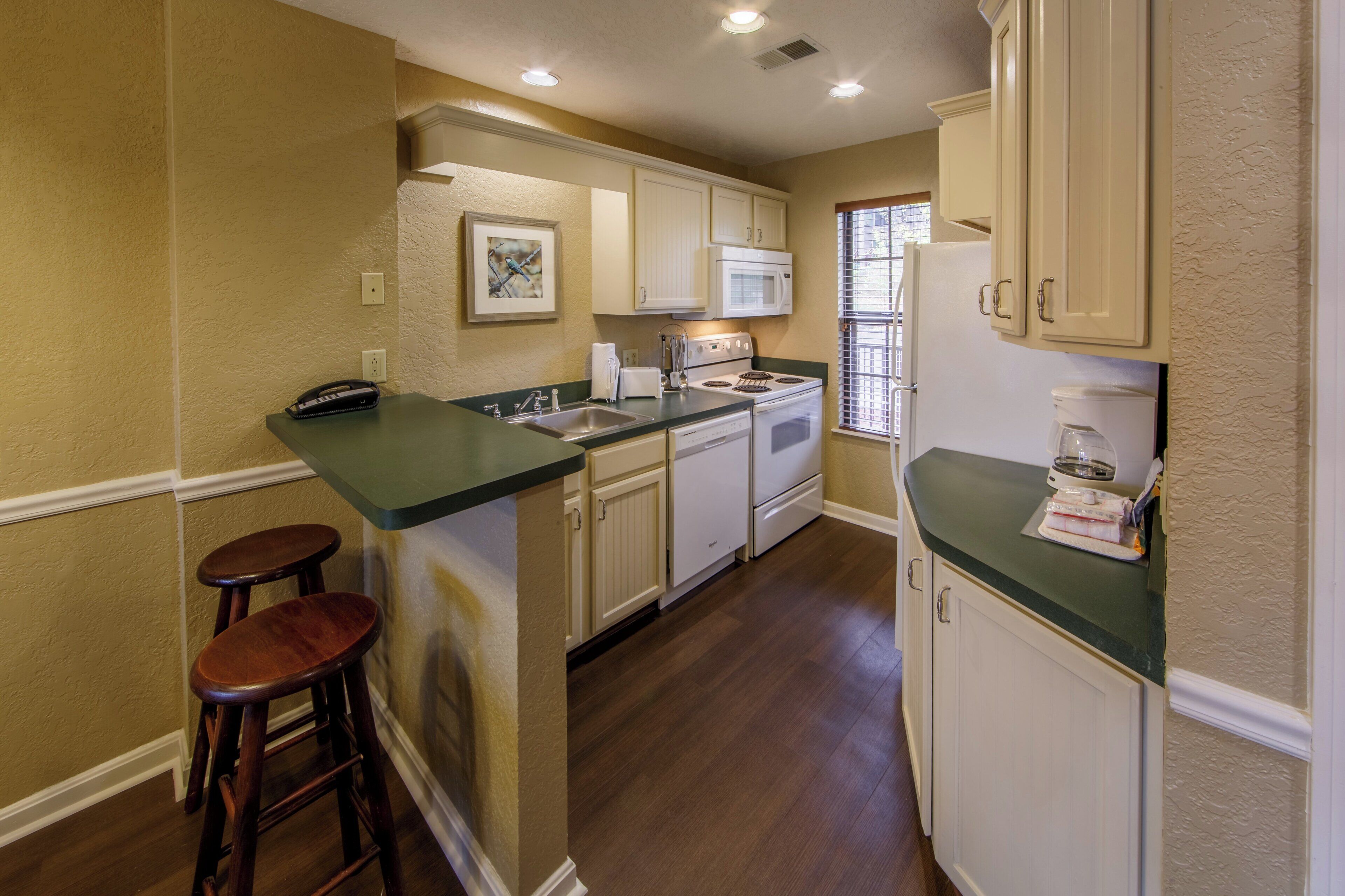 A kitchen with a central island, wooden stools, white cabinets, and a window with blinds.