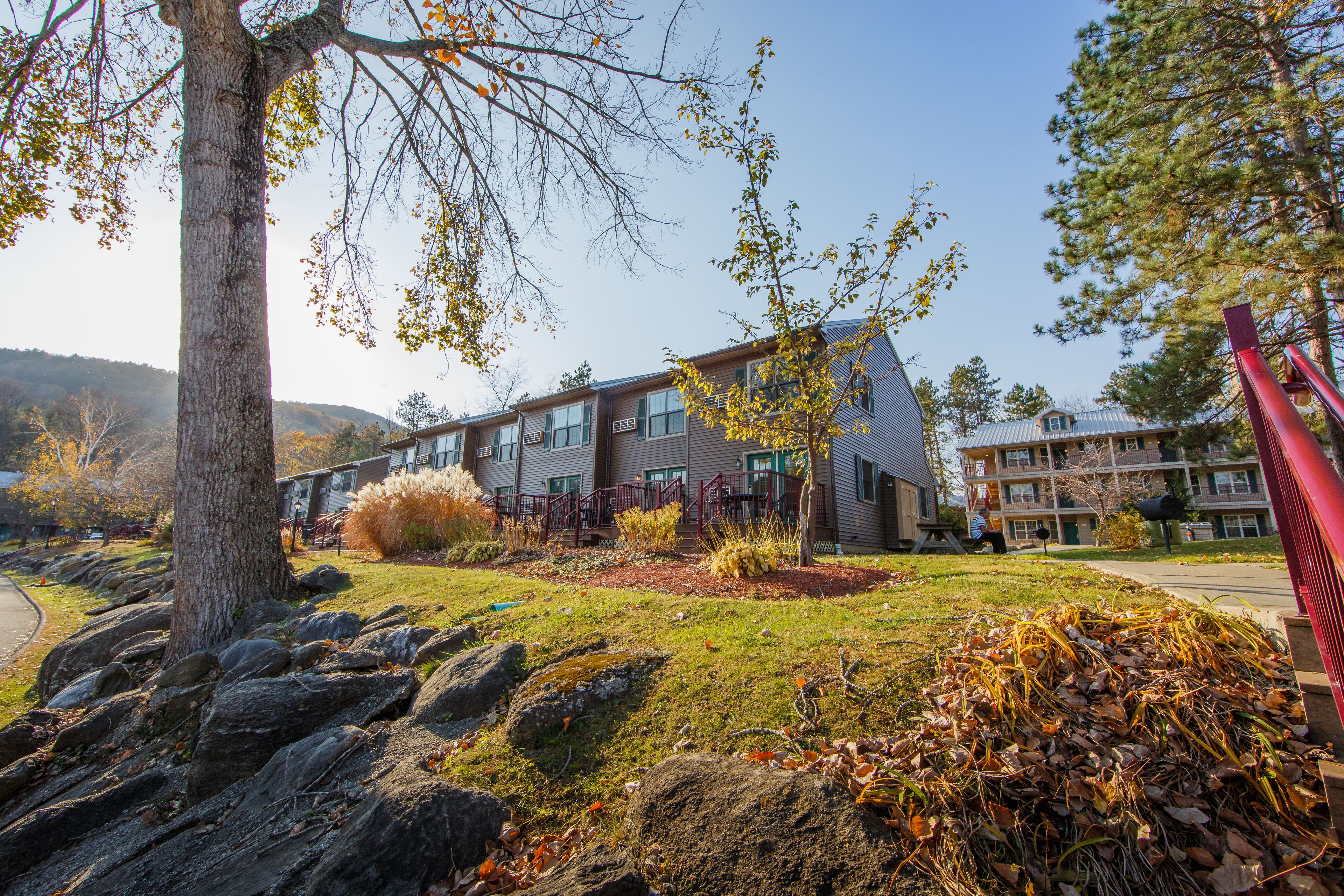 A multi-story building with a modern design, featuring a mix of glass and metal exterior, surrounded by a landscaped garden with rocks and trees.