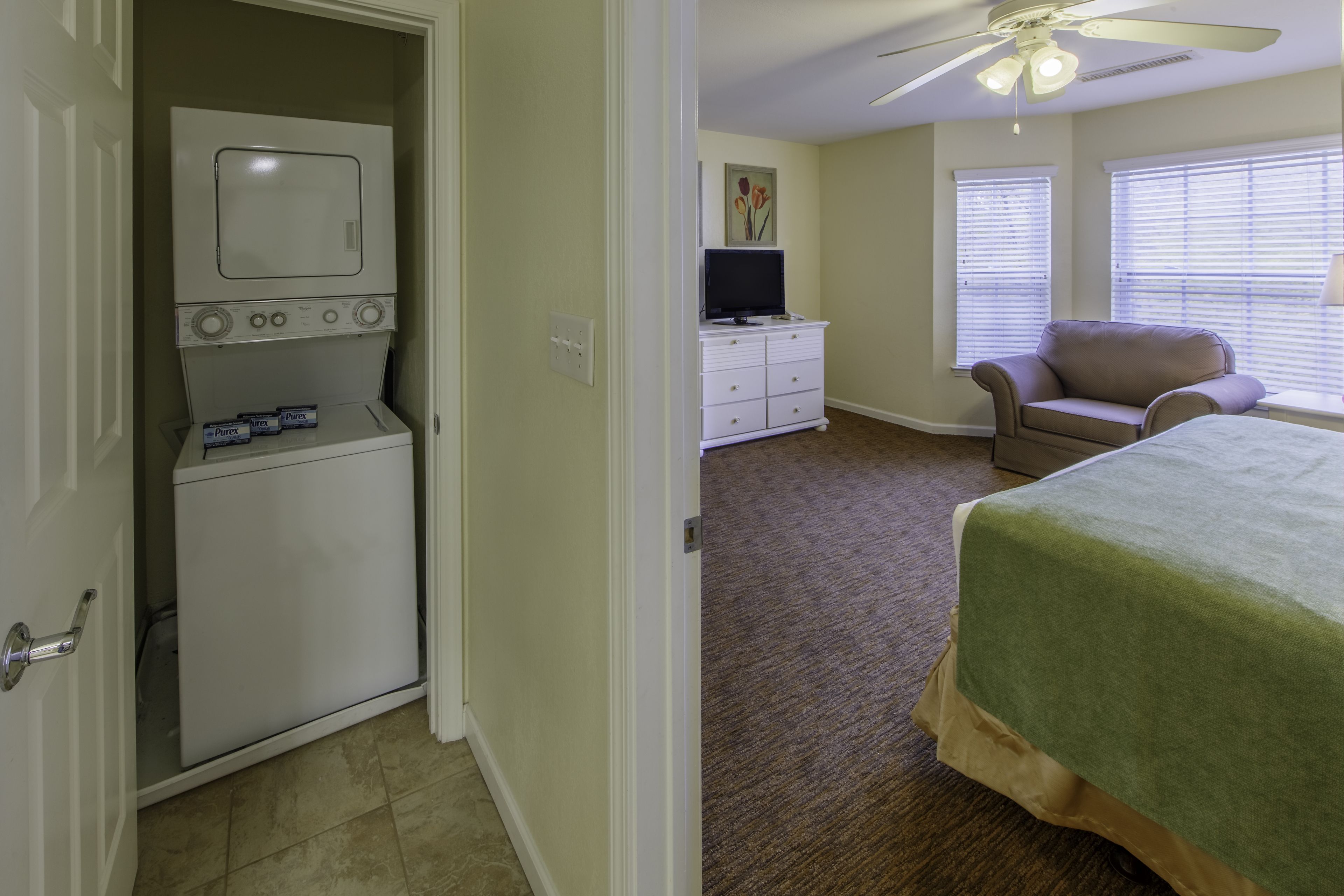Un dormitorio con cama, una silla, un televisor y una lavadora.