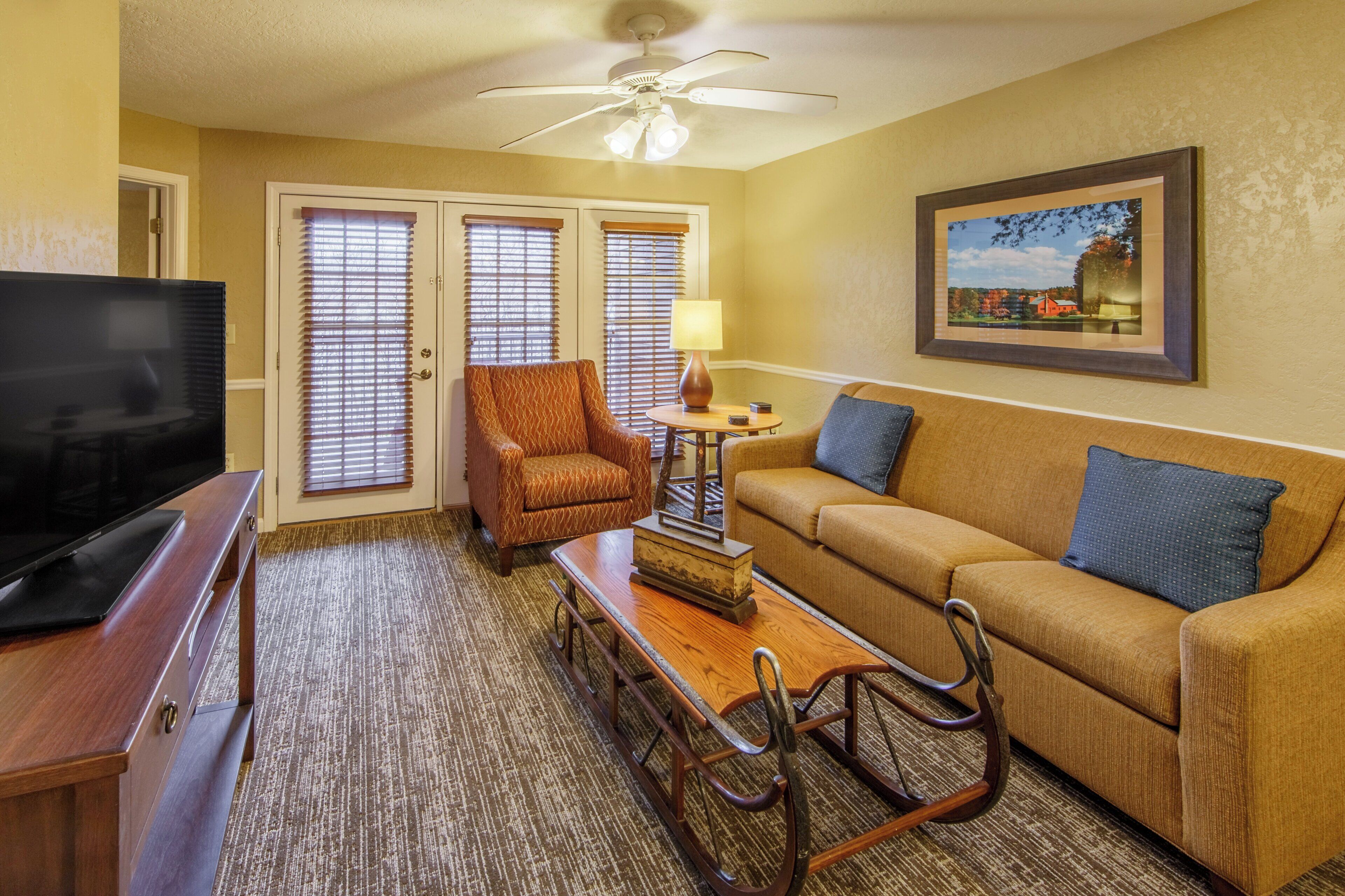 A living room with a television, a sofa, a chair, a table, and a ceiling fan.