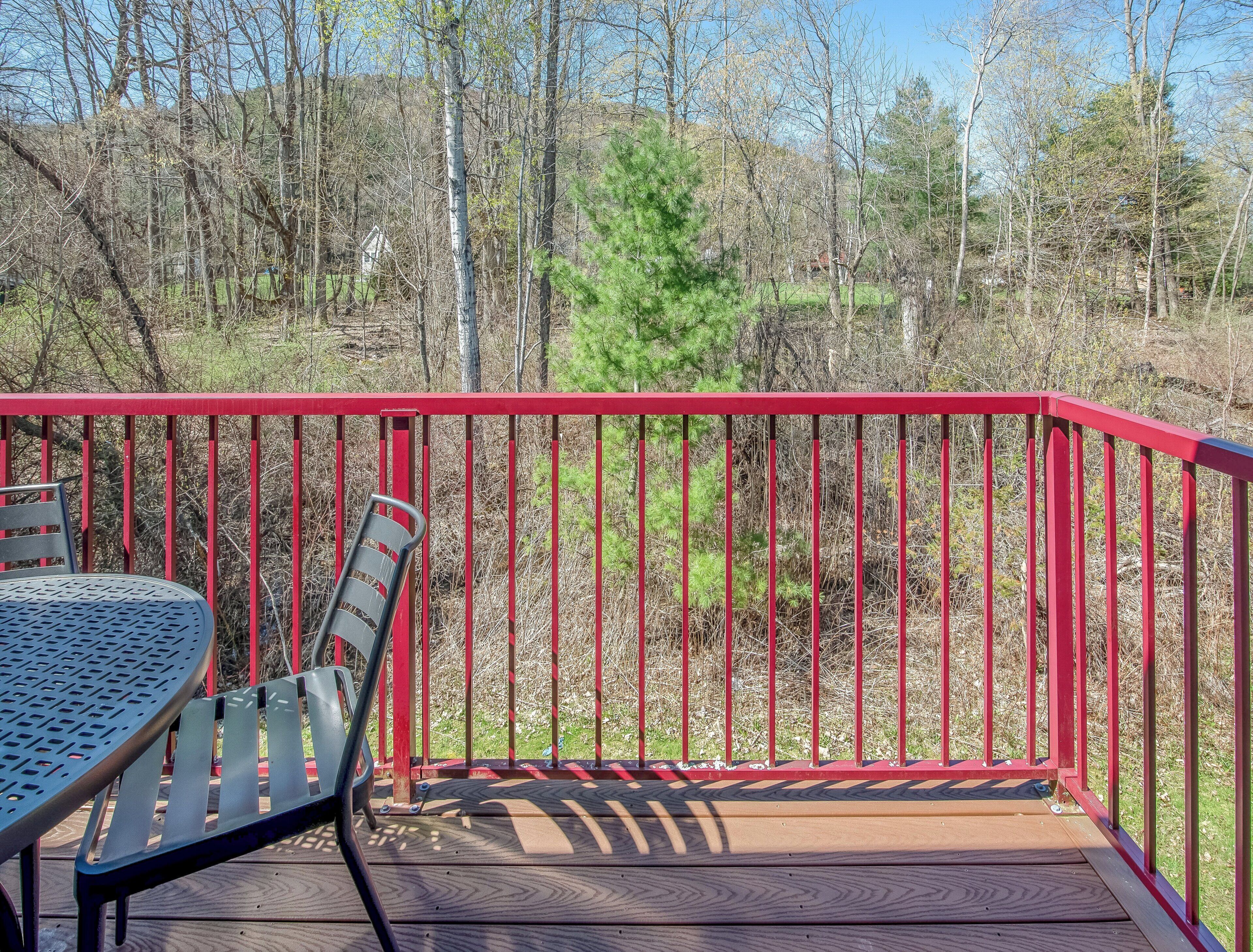 A deck with a red railing, a table, and a chair.
