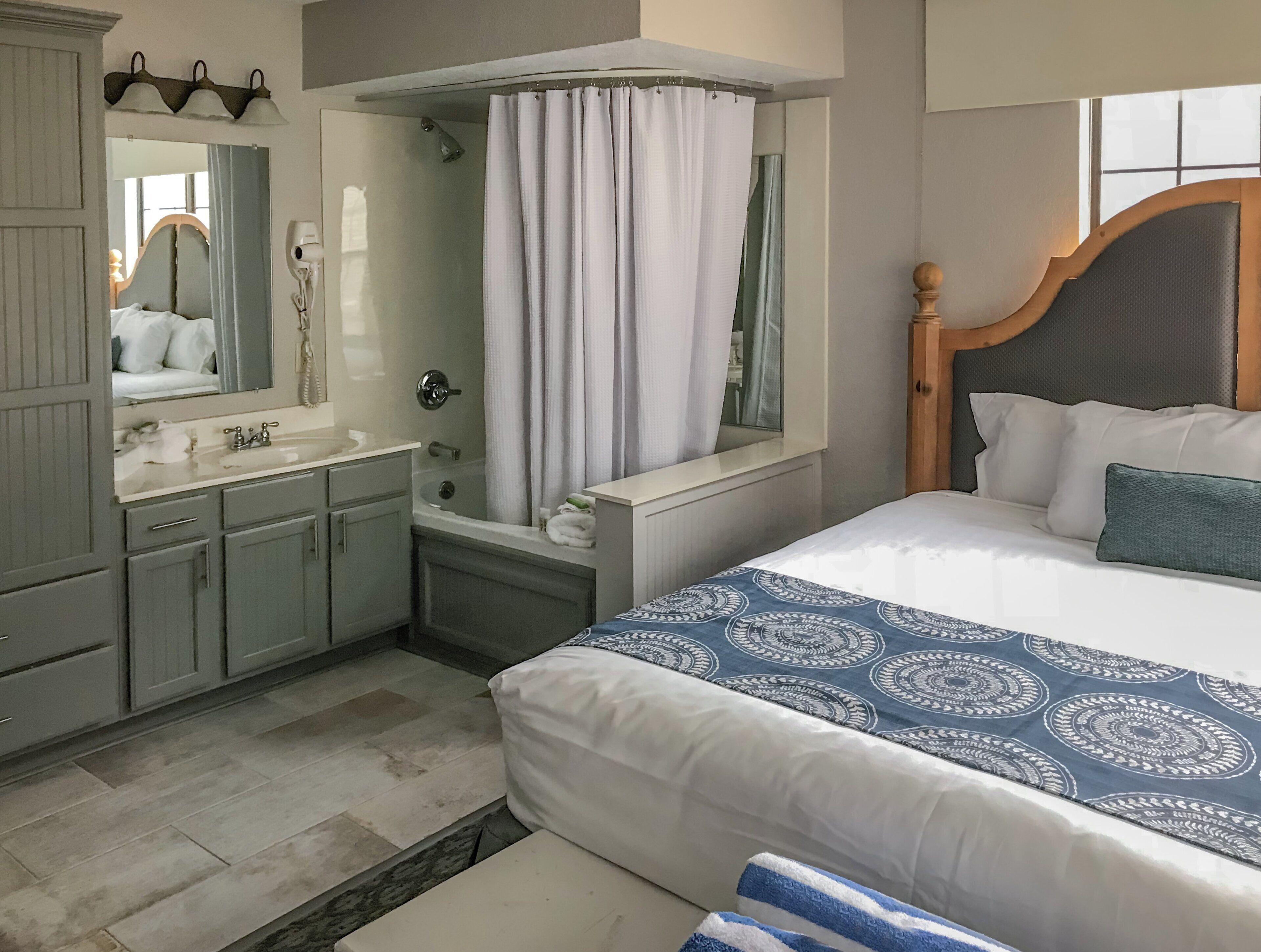 Een hotelkamer met een bed, een badkamer met douche, wastafel en spiegel.