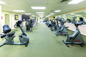 A gym with multiple exercise machines, including treadmills and ellipticals, arranged in rows.