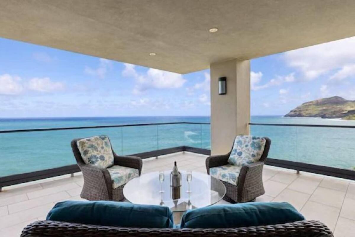 Un balcon offrant une vue dégagée sur l’océan et une île lointaine. On y trouve deux fauteuils en osier et une petite table ronde avec un plateau en verre.